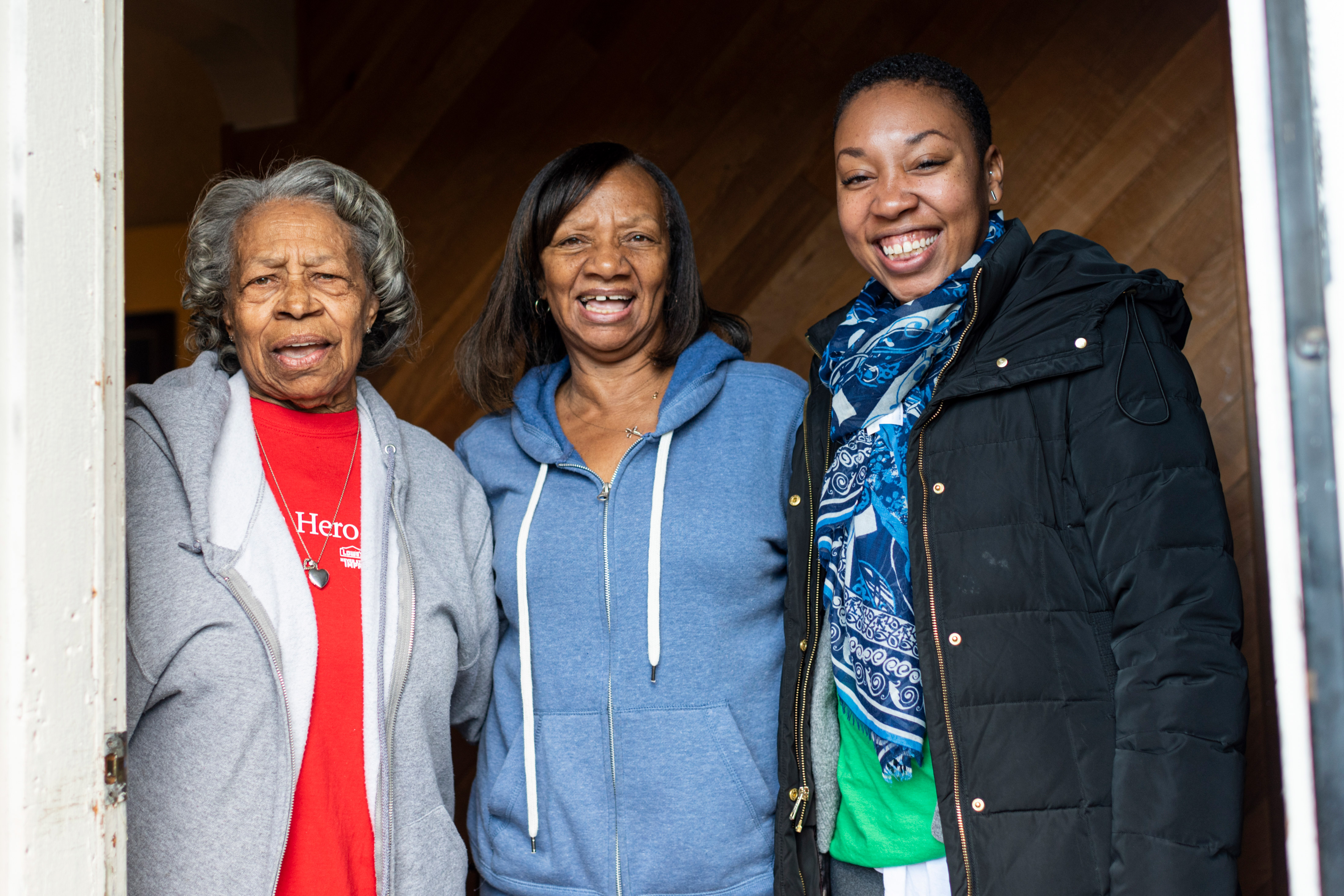 three women standing and smiling in doorway in sweatshirts and coats