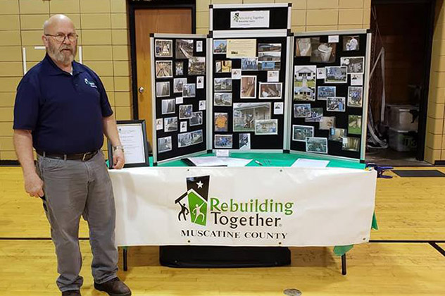 Frank standing in front of a Muscatine County fair table with logo shown.
